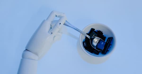 A robotic hand holds a spoon filled with keyboard keys, symbolizing AI and technology fusion.