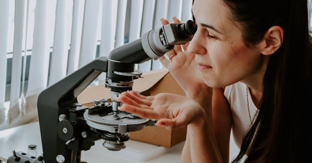 A female researcher examines samples with a microscope in a laboratory setting.