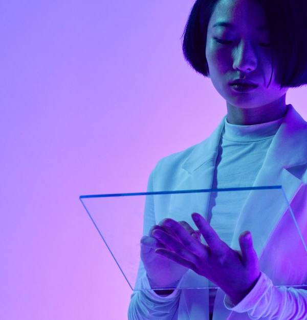 Woman interacts with a transparent digital screen in vibrant studio lighting.