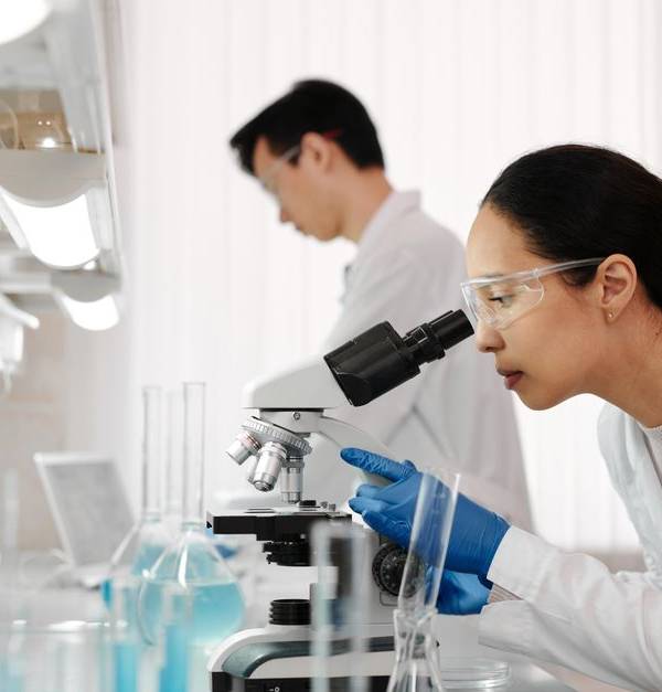 Two scientists in a lab examining samples with a microscope. Focus on scientific research and discovery.