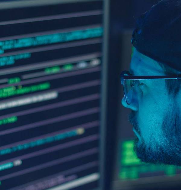 A cybersecurity expert inspecting lines of code on multiple monitors in a dimly lit office.