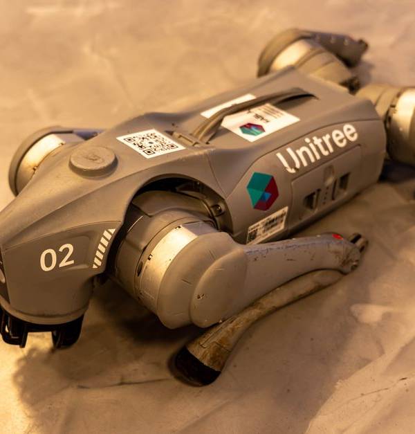A Unitree robot dog resting on an indoor concrete floor.