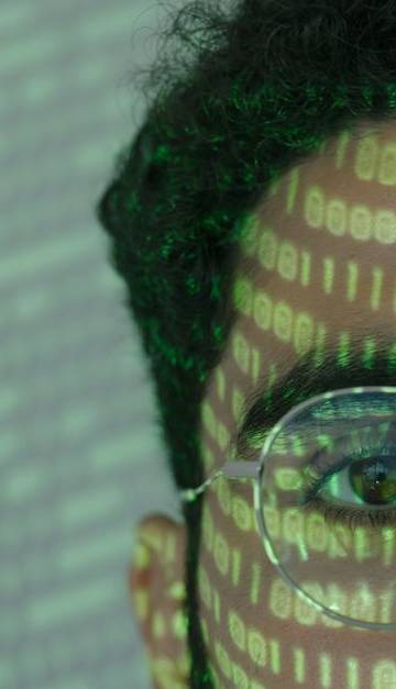 Close-up of a man with binary code projected on his face, symbolizing cybersecurity.