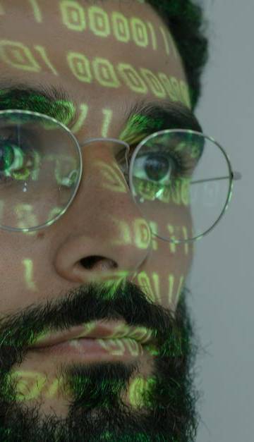 A bearded man with digital binary code projected on his face, symbolizing cybersecurity and technology.