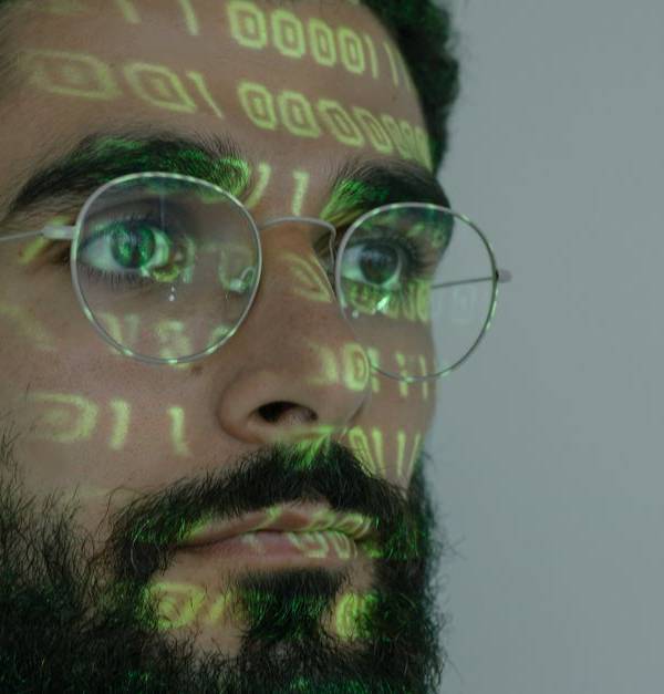 A bearded man with digital binary code projected on his face, symbolizing cybersecurity and technology.