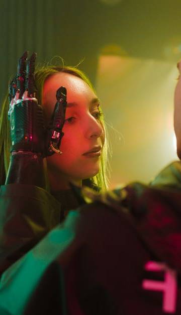 A man with a prosthetic hand gently touches a woman's face in a cyberpunk setting.