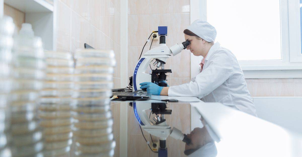 Female scientist using a microscope in a laboratory environment, focusing on research.