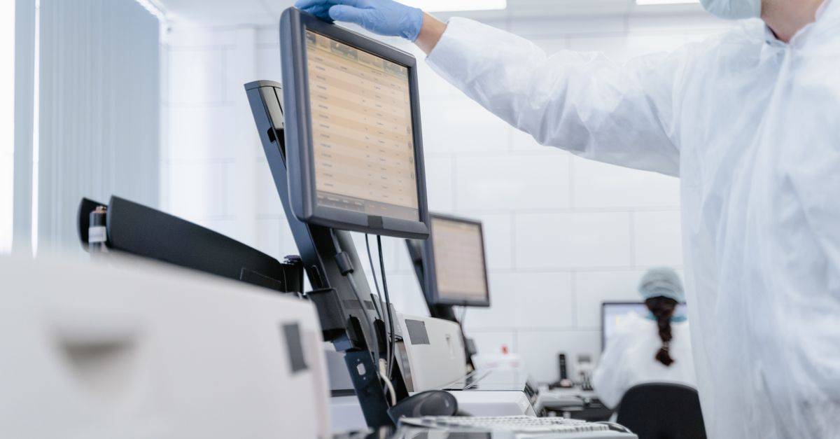 Researcher in PPE reviews data on a digital screen in a modern laboratory setting.