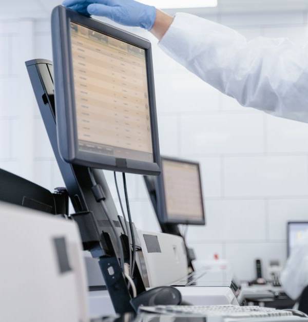 Researcher in PPE reviews data on a digital screen in a modern laboratory setting.