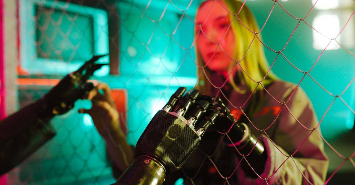 A woman interacts with a robotic hand through a fence under neon lights.