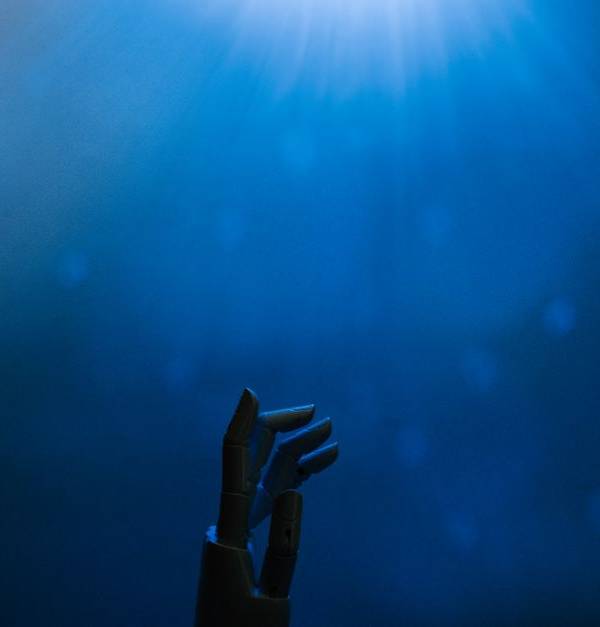 Silhouette of a robotic hand reaching towards glowing blue light in a futuristic setting.