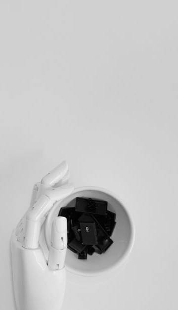 A robotic hand grasping black keyboard keys in a minimalist setting.