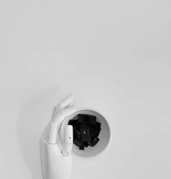 A robotic hand grasping black keyboard keys in a minimalist setting.