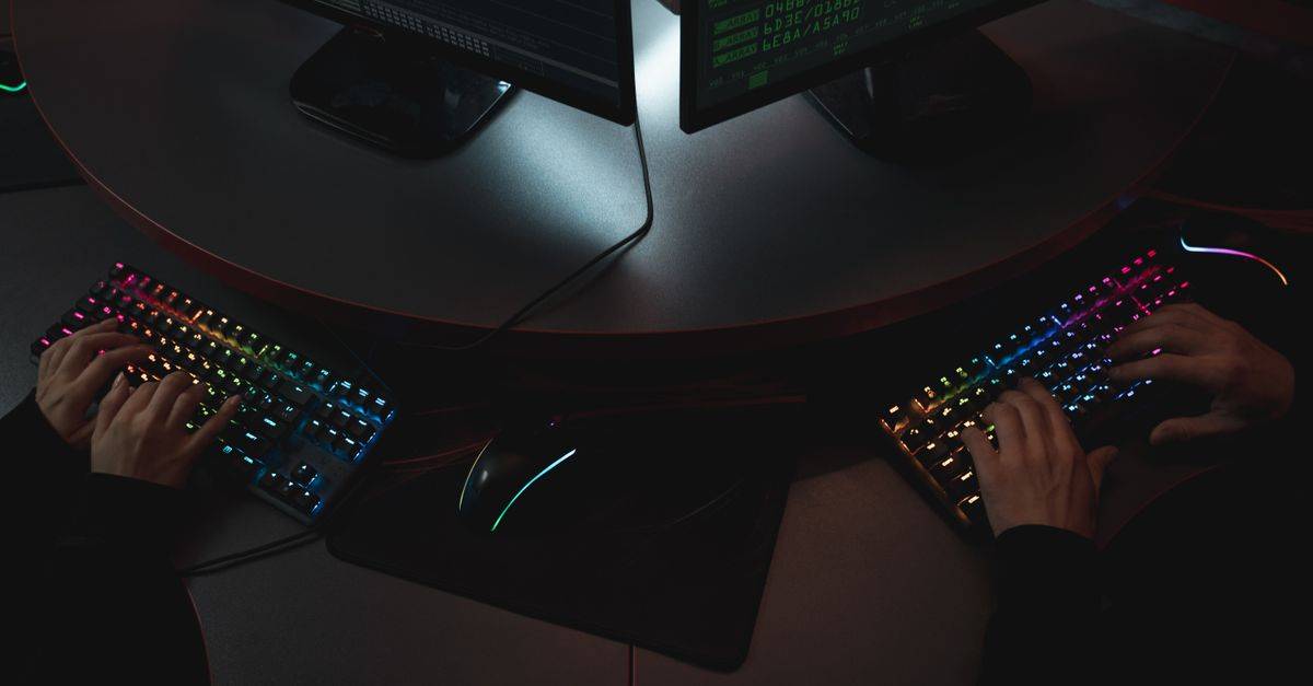 Two people typing on RGB keyboards with code on screens, indicating a cybersecurity environment.