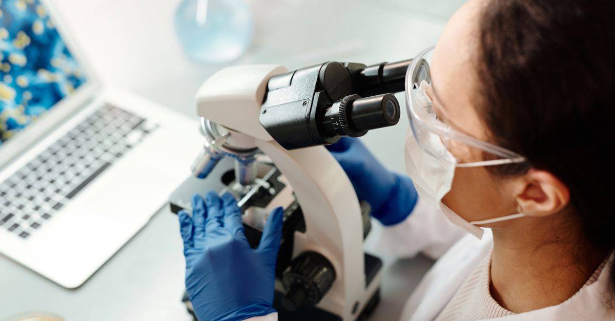 Scientist in protective gear examining samples with microscope in laboratory setting.