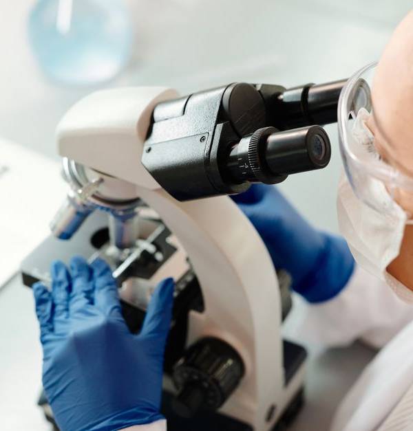 Scientist in protective gear examining samples with microscope in laboratory setting.