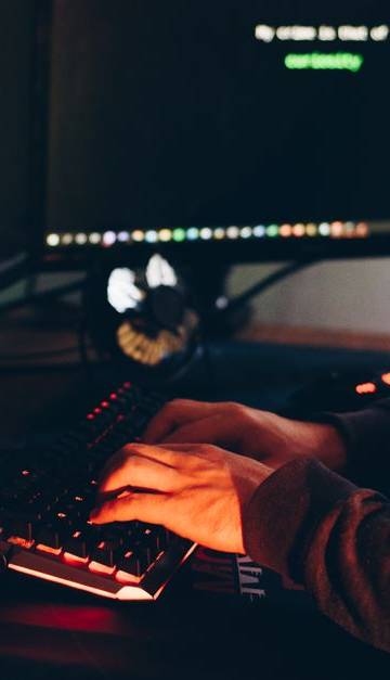 Side view of crop anonymous male cyber thief accessing information on desktop computer screens at dusk