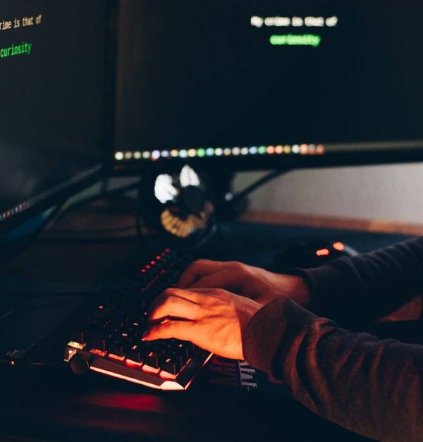 Side view of crop anonymous male cyber thief accessing information on desktop computer screens at dusk