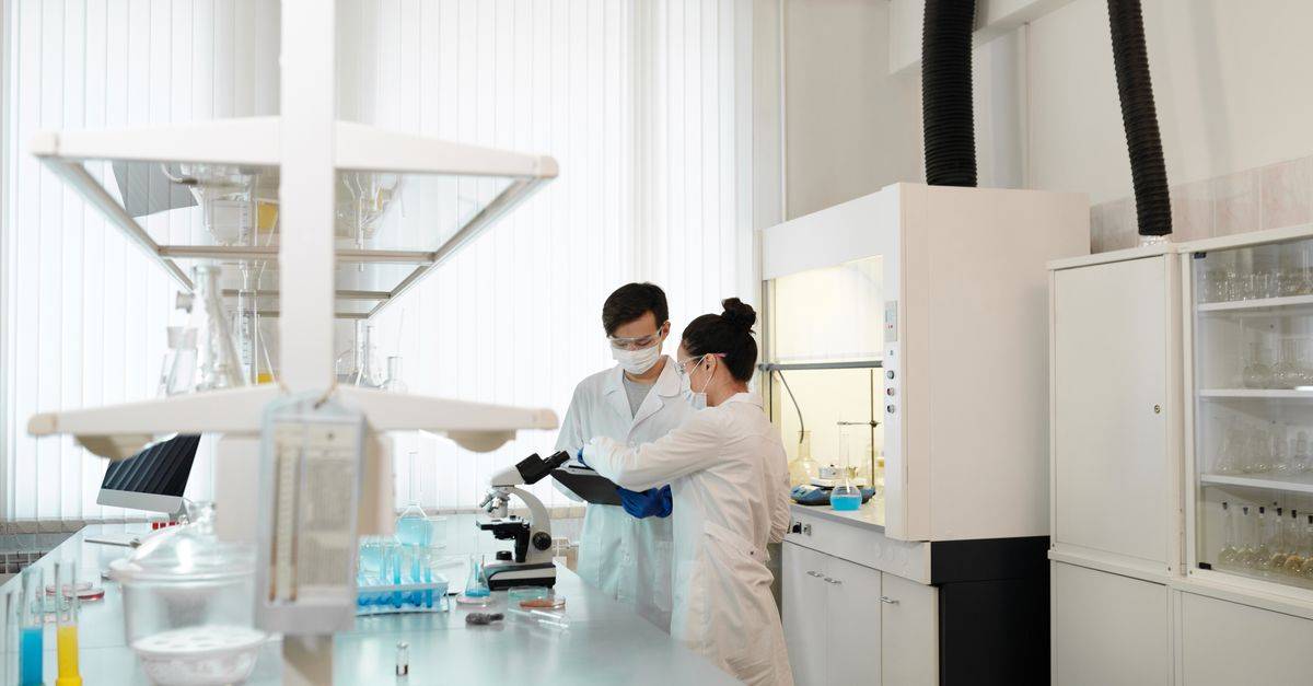 Two scientists wearing protective gear collaborating in a laboratory setting with modern equipment.