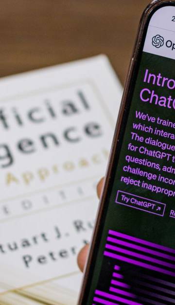 Close-up of a smartphone displaying ChatGPT app held over AI textbook.
