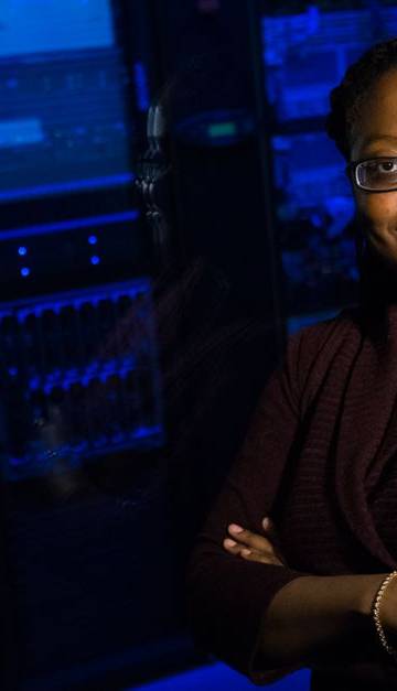 Professional woman standing confidently in a data center, surrounded by glowing servers.