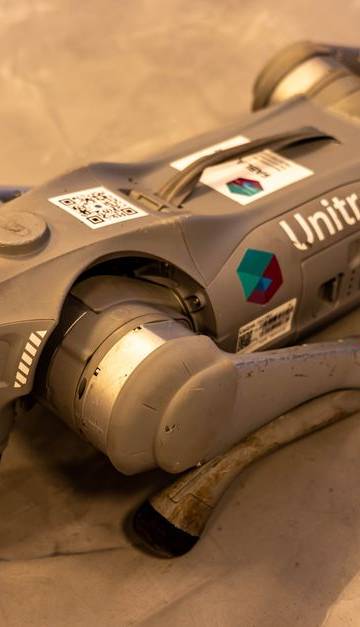 A Unitree robot dog resting on an indoor concrete floor.