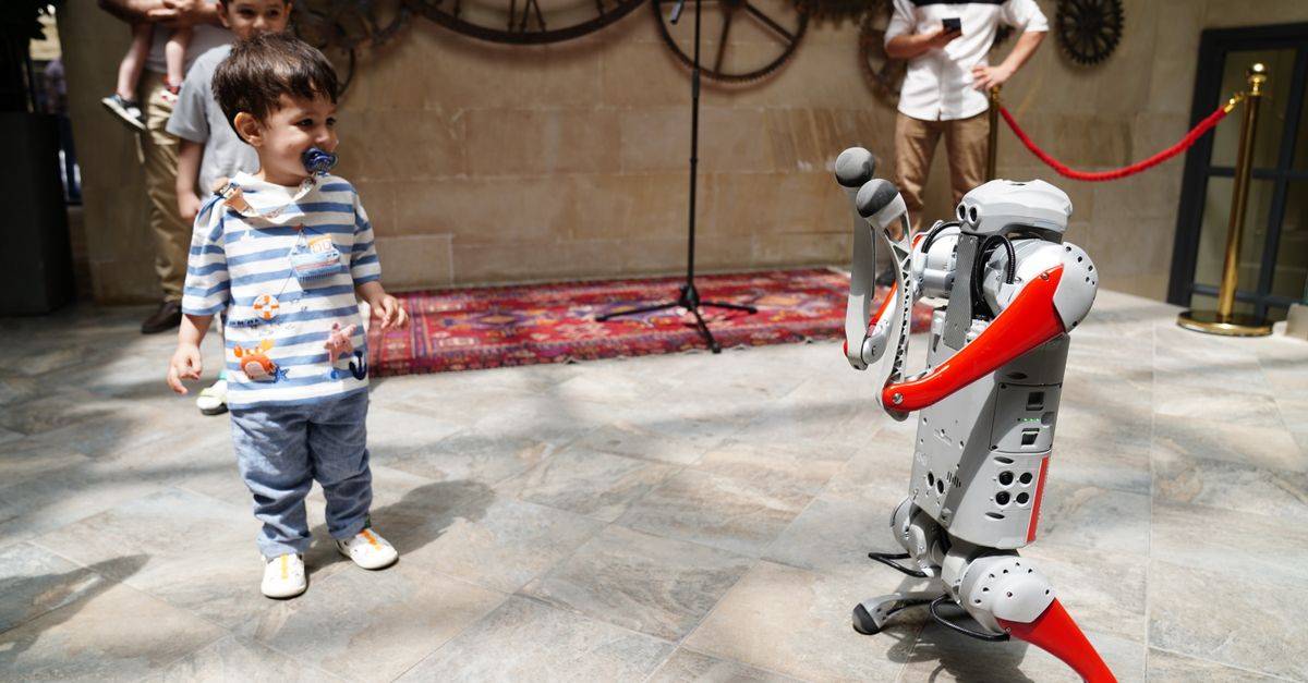 A young boy engages with a humanoid robot during an indoor tech exhibition, symbolizing future innovation.