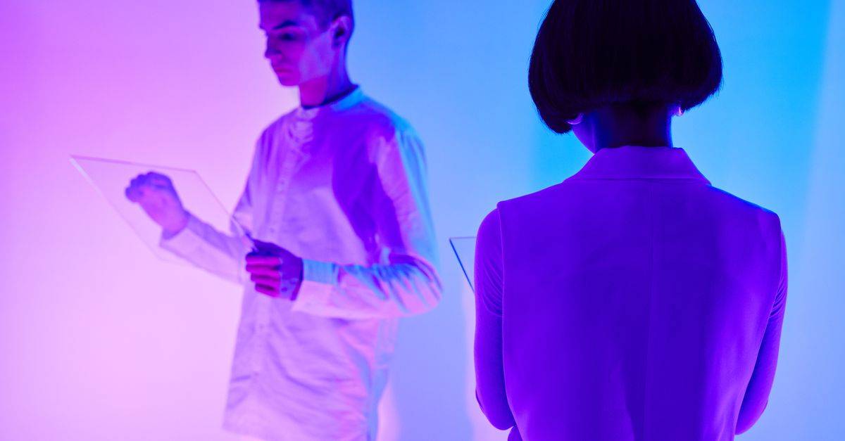 Two individuals interact with digital interfaces in a colorful futuristic setting.