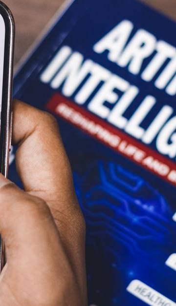Smartphone displaying AI app with book on AI technology in background.