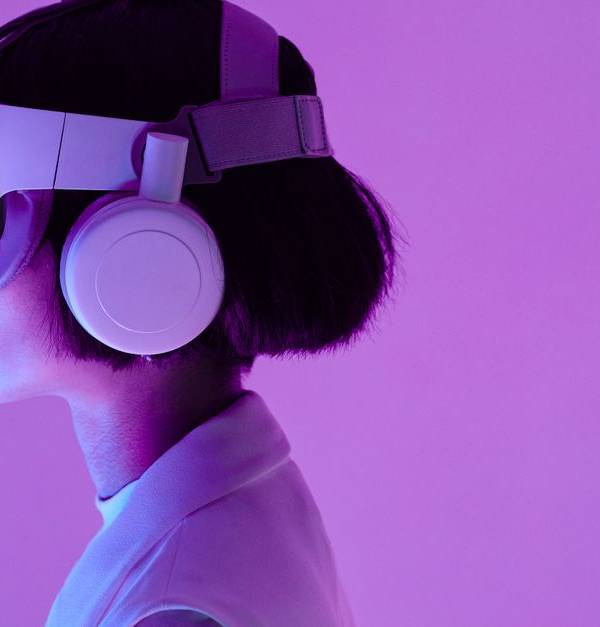 Side view of a woman wearing VR goggles in a purple-lit studio, highlighting modern technology.