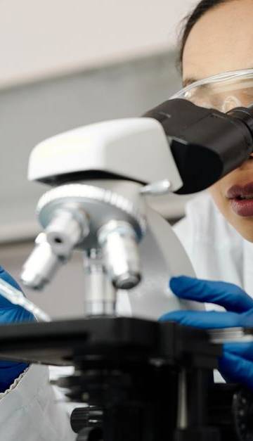 A female scientist examines samples using a microscope in a laboratory setting.