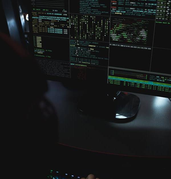Dark room setup with code displayed on PC monitors highlighting cybersecurity themes.