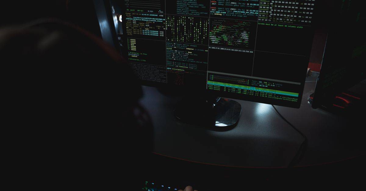 Dark room setup with code displayed on PC monitors highlighting cybersecurity themes.