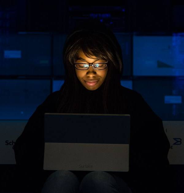 A woman uses her laptop in a dimly lit server room, focusing on technology and work.