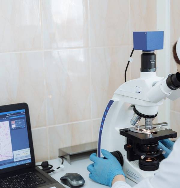 Scientist in lab coat using microscope and laptop in a laboratory setting.