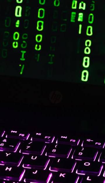 Illuminated laptop keyboard with Matrix-style green code cascading down screen.