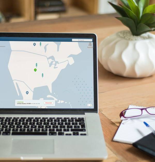 A laptop displaying VPN software sits on a wooden desk with a notepad and plant offering a secure workspace vibe.