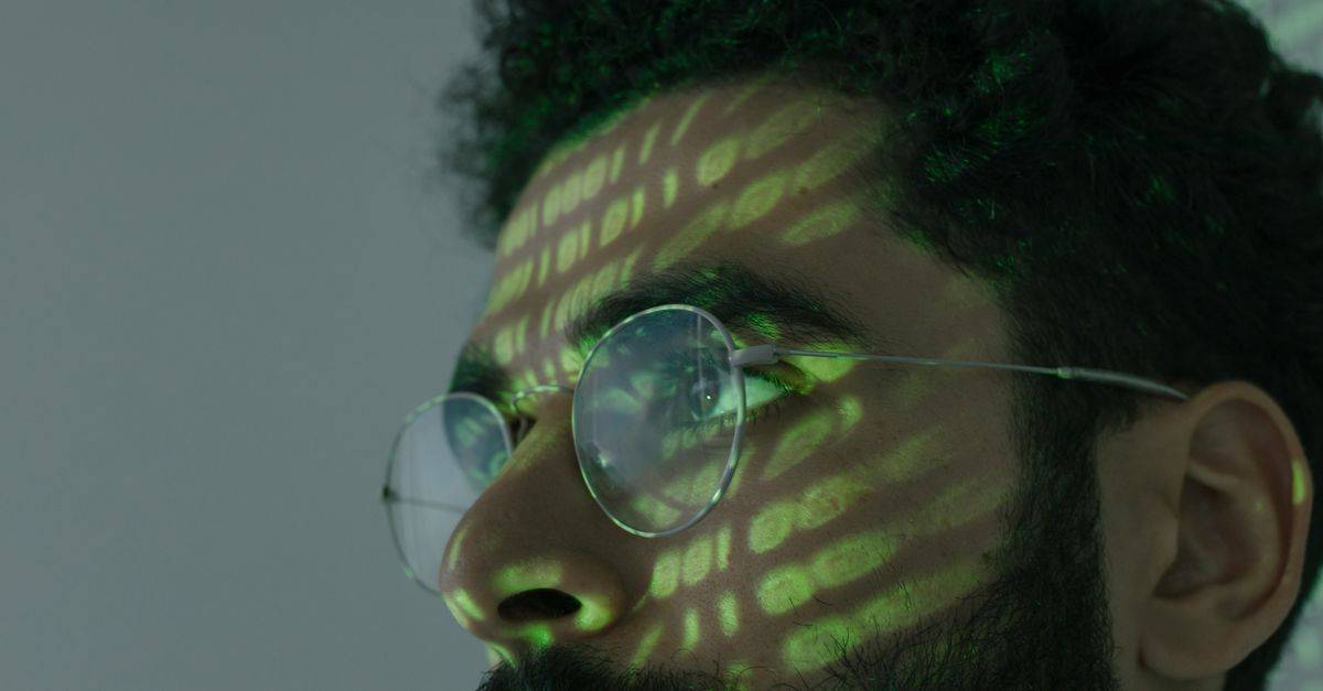 A man wearing glasses with binary code projected across his face, symbolizing cybersecurity.