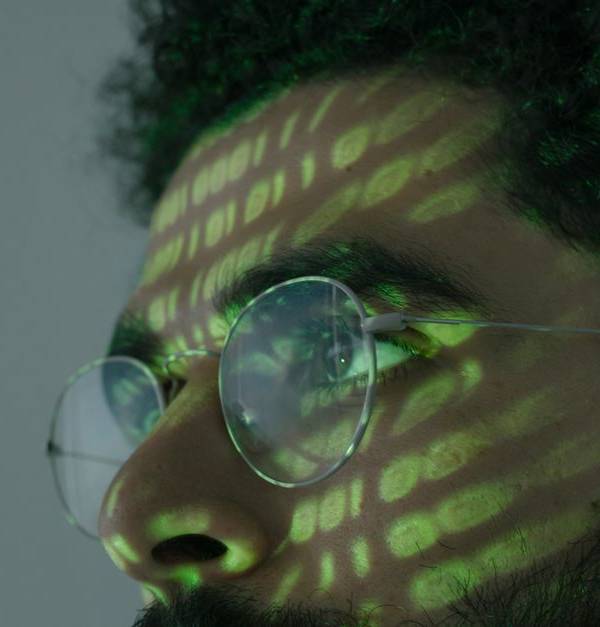 A man wearing glasses with binary code projected across his face, symbolizing cybersecurity.