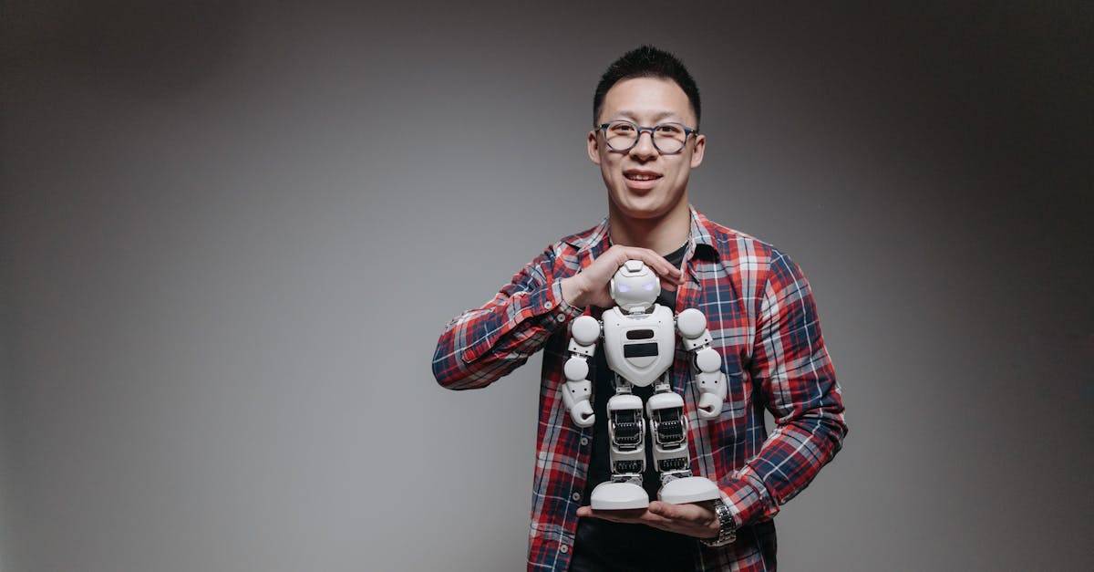Asian man with eyeglasses holding a toy robot in a studio with a gray background.