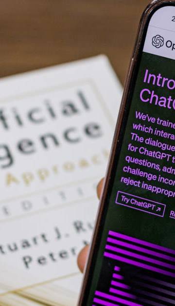 Close-up of a smartphone displaying ChatGPT app held over AI textbook.