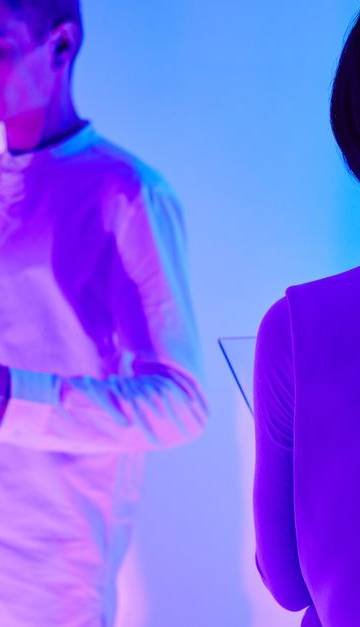 Two individuals interact with digital interfaces in a colorful futuristic setting.