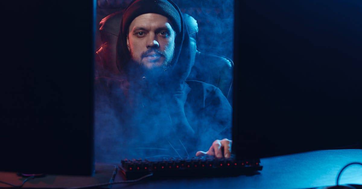 Dramatic scene of an adult man in a hoodie using a computer, surrounded by smoke in a dimly lit room.