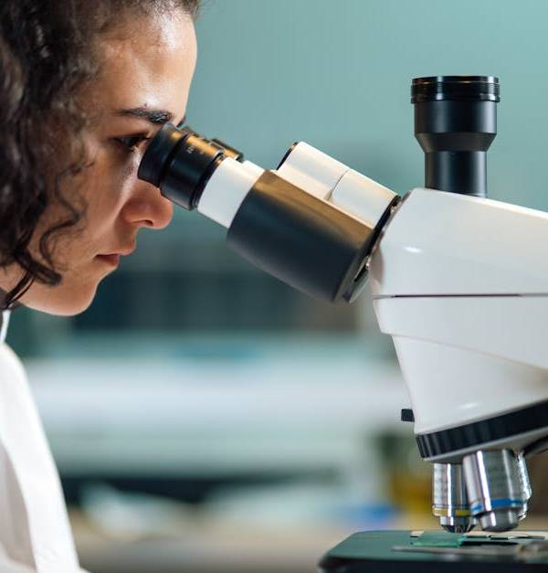 A focused scientist examines samples under a microscope in a laboratory setting.