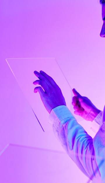 Two individuals engaging with futuristic transparent touch screens in a vibrant purple-lit studio.