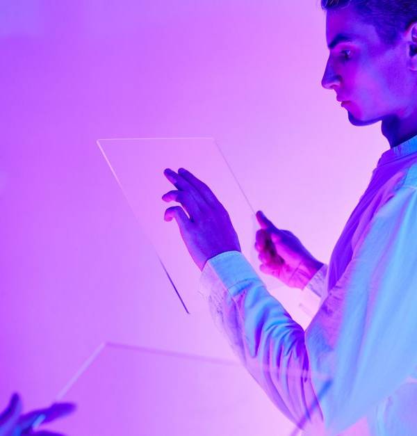 Two individuals engaging with futuristic transparent touch screens in a vibrant purple-lit studio.