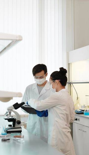 Two scientists wearing protective gear collaborating in a laboratory setting with modern equipment.