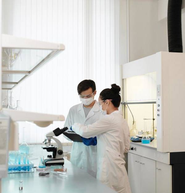 Two scientists wearing protective gear collaborating in a laboratory setting with modern equipment.