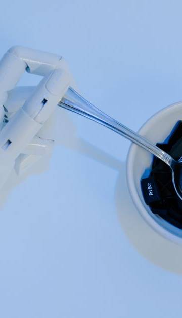 A robotic hand holds a spoon filled with keyboard keys, symbolizing AI and technology fusion.