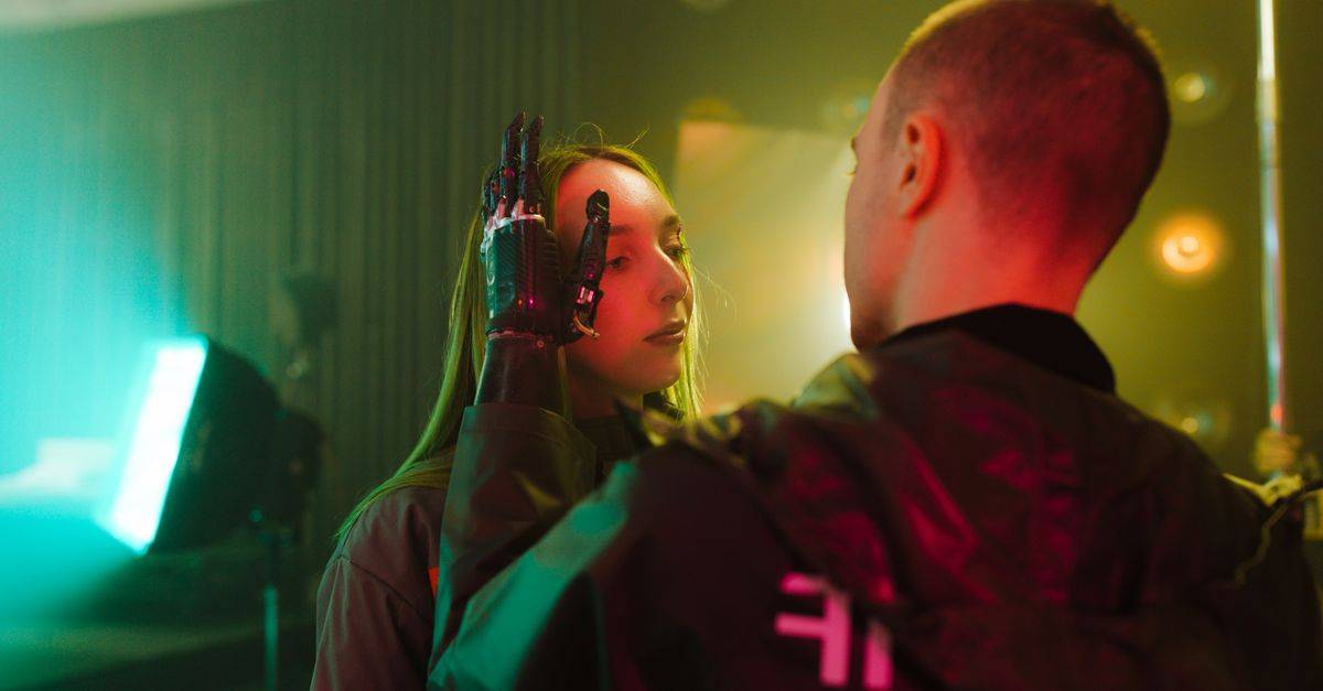 A man with a prosthetic hand gently touches a woman's face in a cyberpunk setting.